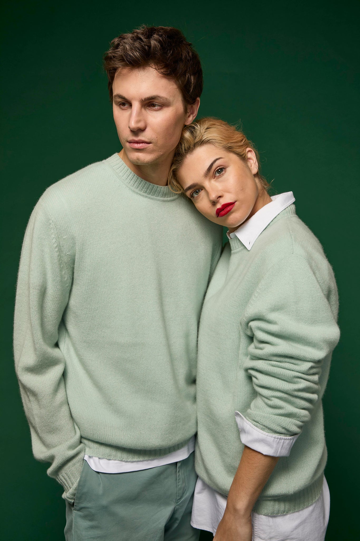 Two people wearing matching light green sweaters against a dark green background