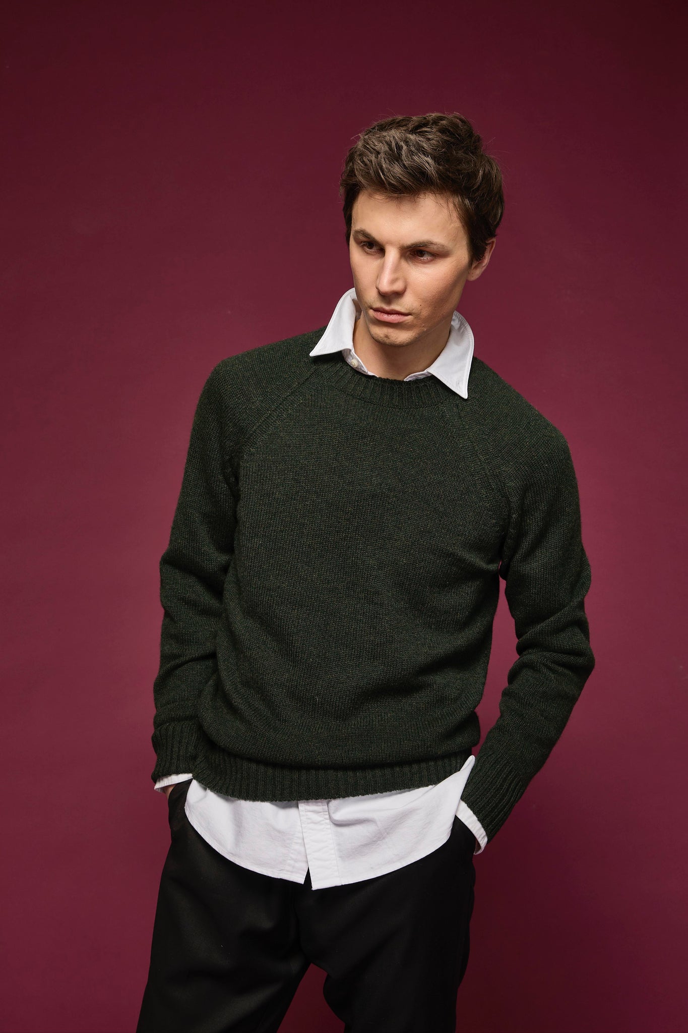 Man wearing a dark green sweater over a white shirt on a purple background