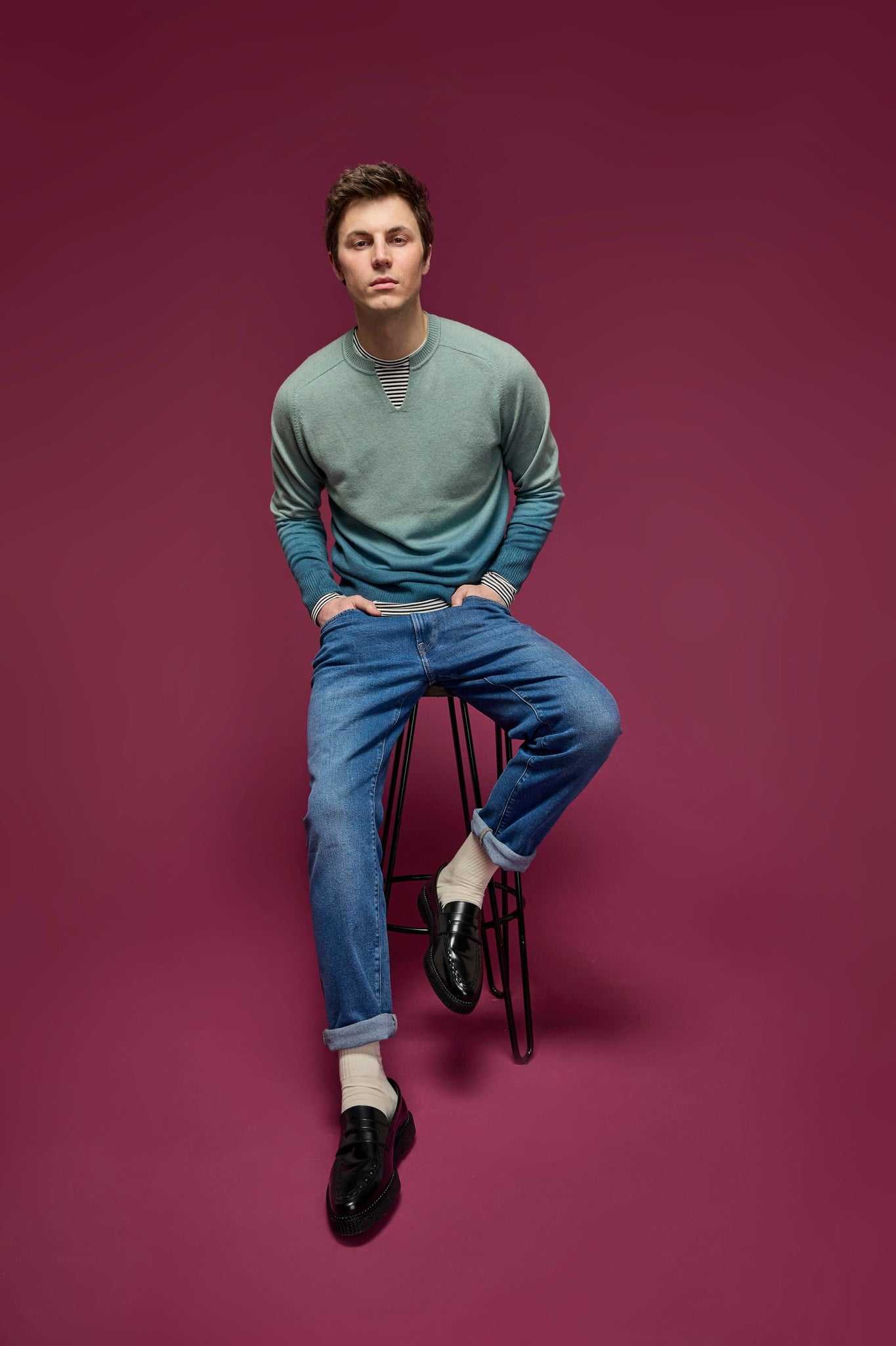 Man sat on a stool wearing a dip-dye green and teal sweater