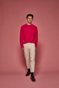 Man wearing a bright pink sweater and beige pants against a pink background
