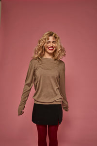 Woman wearing a brown sweater and black skirt against a pink background